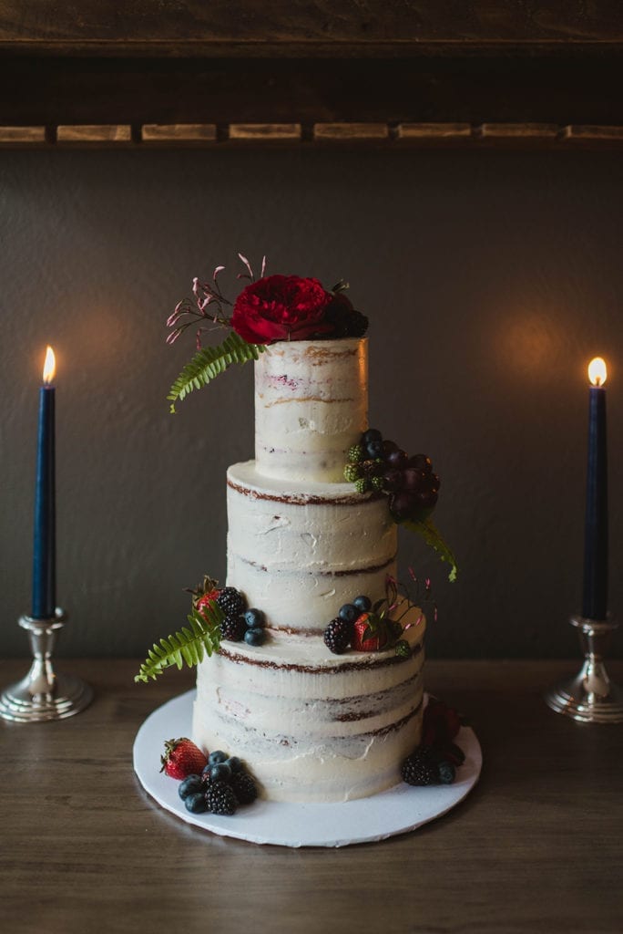 naked cake decorated with berries and jewel-toned flowers